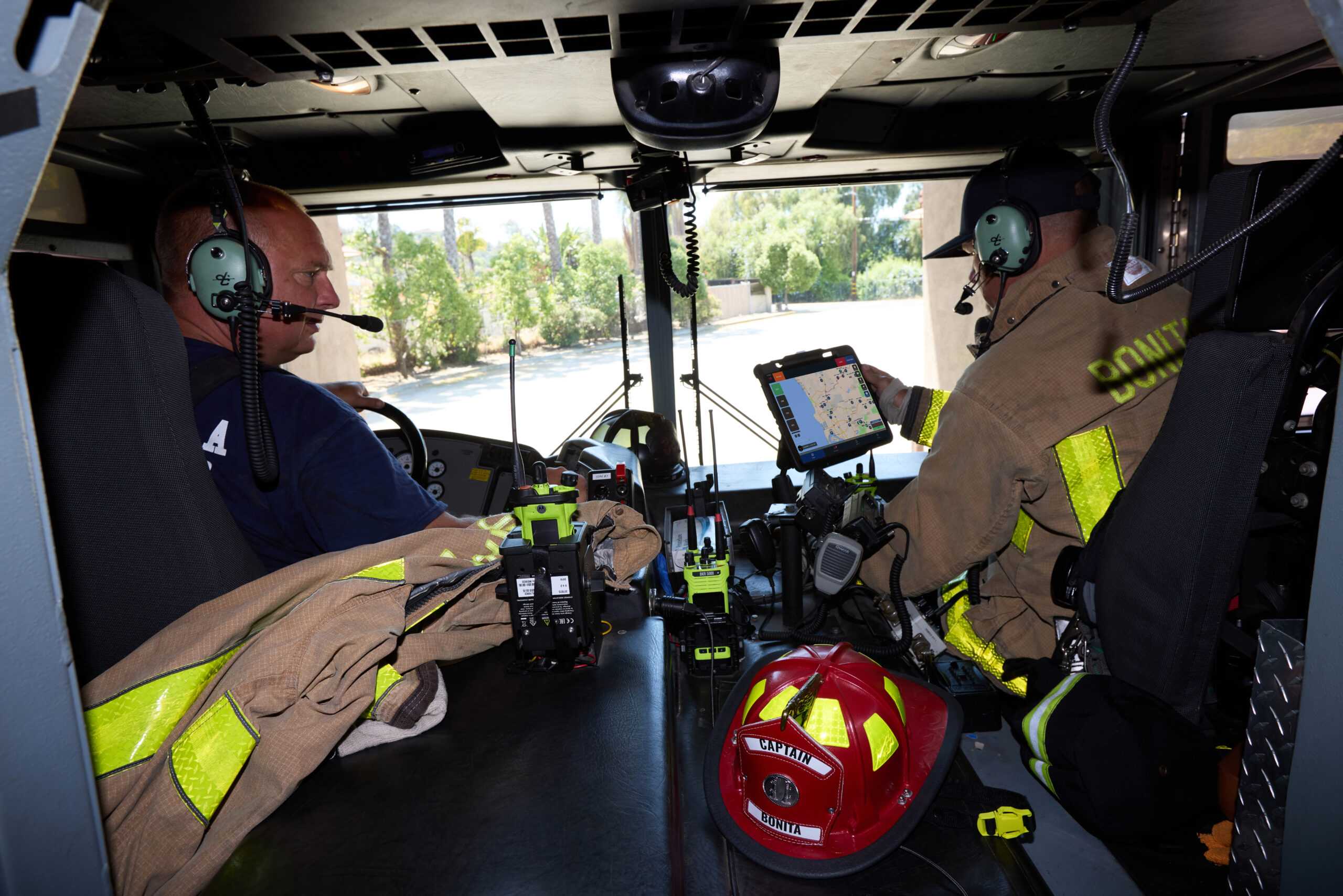 Bonita Fire Department captain and crew member inside a fire engine cab reviewing an AVL mapping system on a tablet, surrounded by communication radios and equipment