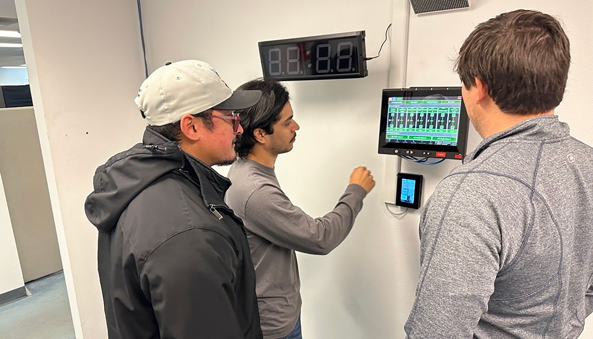 RMI Careers Team Collaboration and Technology Three RMI employees collaborating around a wall-mounted technology display showing a system interface.